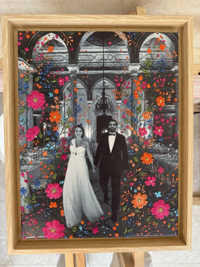 Wood-framed black-and-white wedding portrait surrounded by vivid pink, orange and blue embroidered flowers